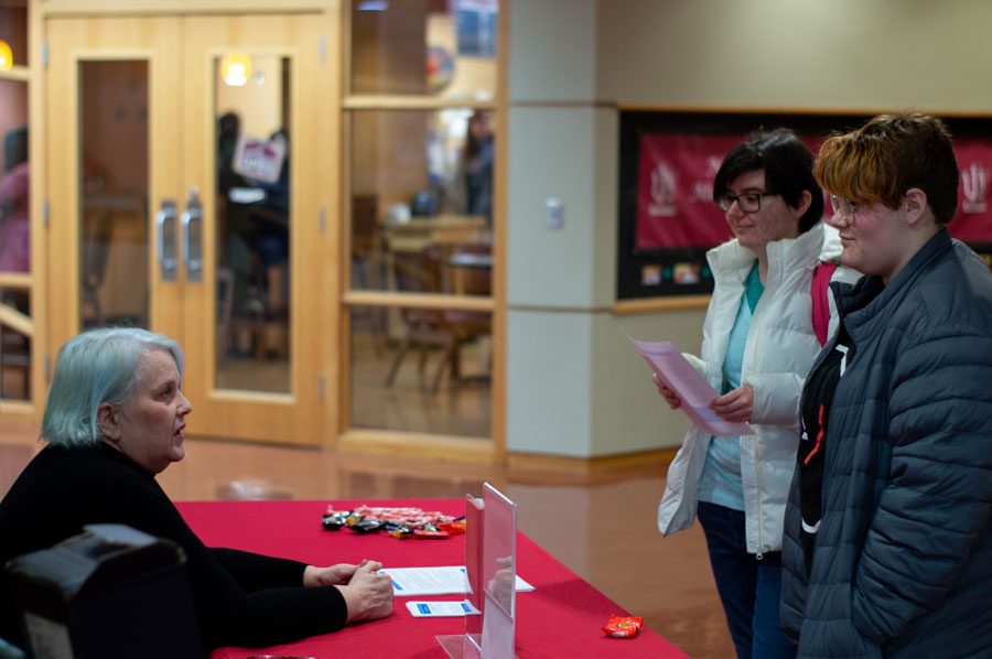 Anita+Kraft+answers+questions+posed+by+freshmen+Holly+Britton+and+Larissa+Dalton+about+the+autism+group+meeting.+Kraft+set+up+a+table+in+the+hallway+at+noon+during+the+first+week+of+classes+to+raise+awareness+for+her+new+group.